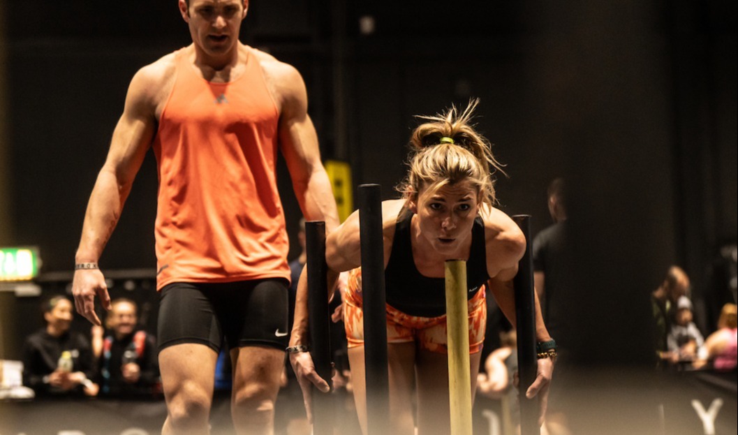 Female team member pushing a sled and male team member supporting at HYROX event