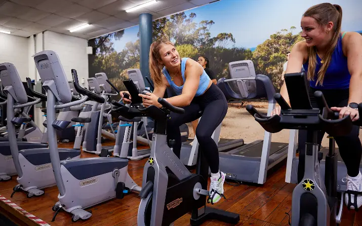 Two young females smiling whilst cycling at Perth HPC Gym