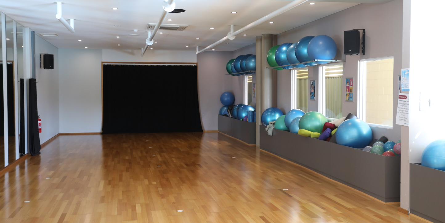 A photo of an empty wooden floor room with exercise and balance balls stored on the right side