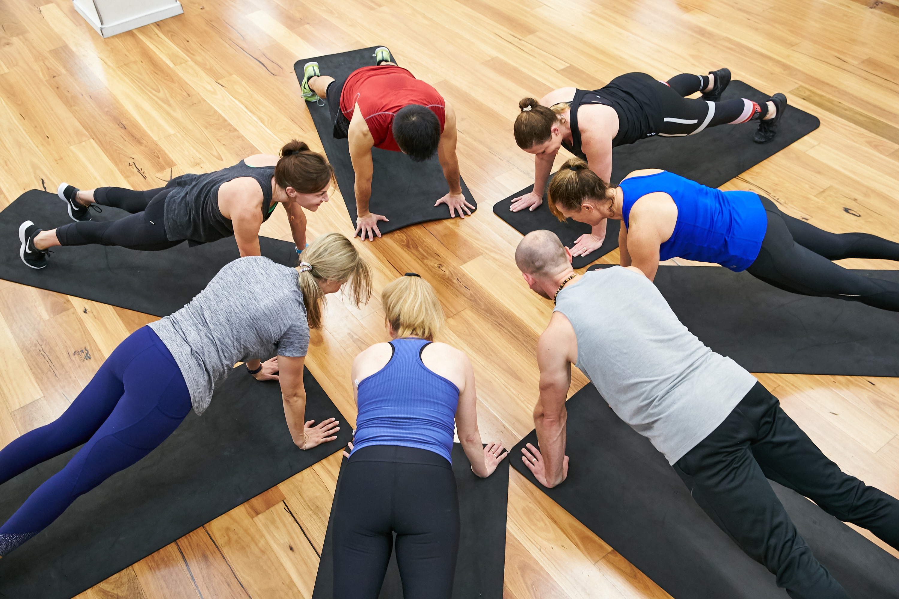 A group of six fitness class participants forming a circle on the floor