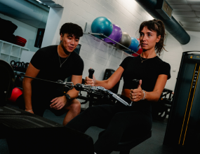 Female member on rowing equipment at Perth HPC Gym with male member kneeling in support