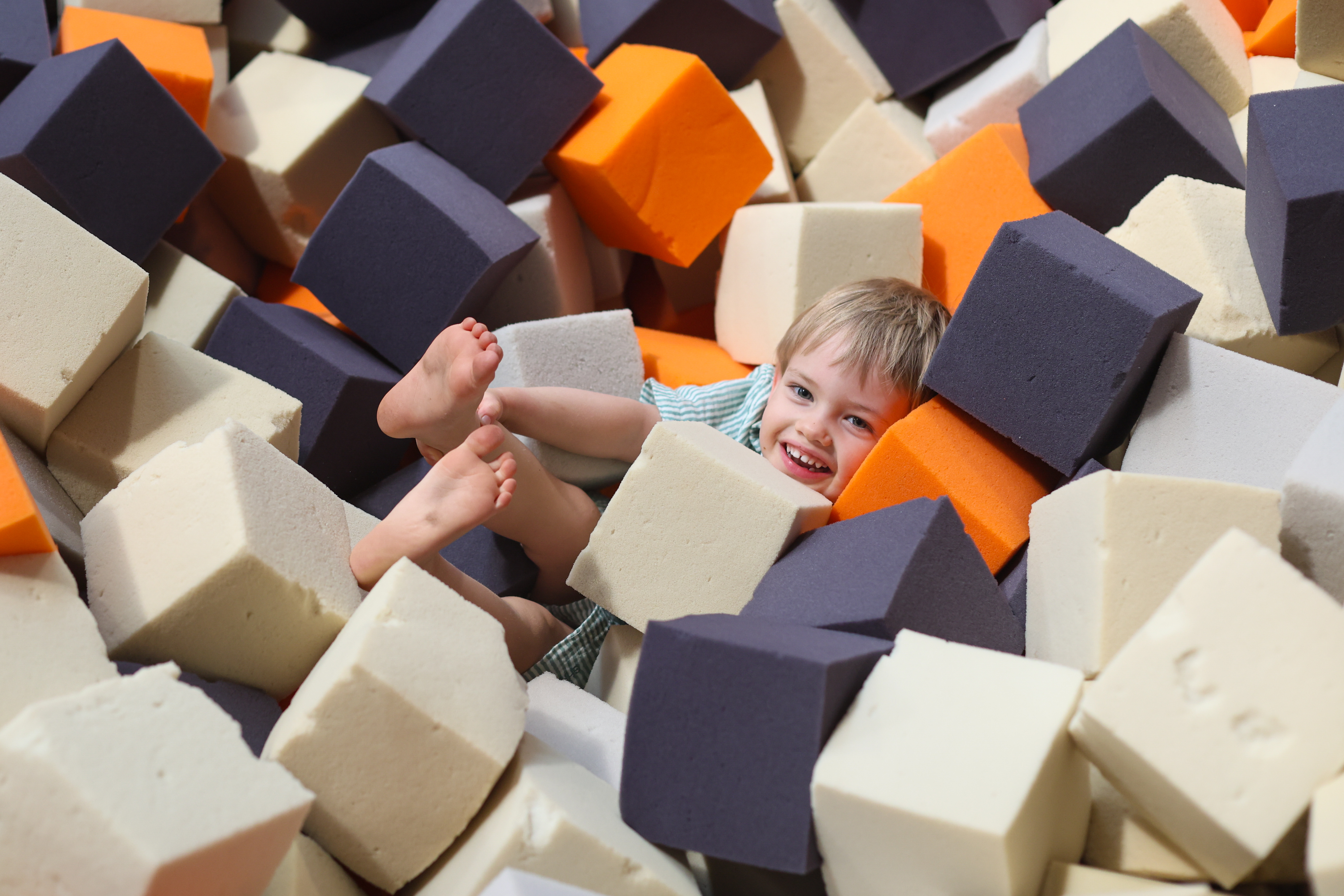 Young boy smiling at camera whilst submerged in foam pit in the Gymnastics Training Centre at Perth HPC, Mount Claremont