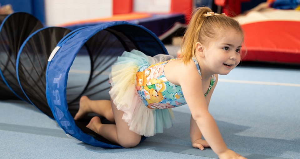 Young girl crawling through play tunnel at kids gymnastics