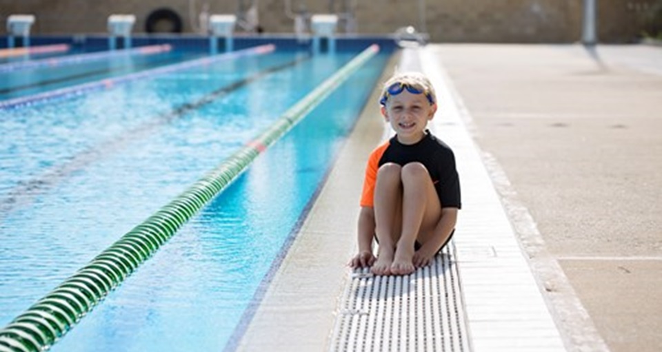 Young boy sitting on the pool edge looking unsure about getting in
