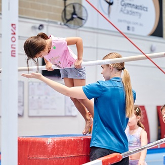 Photo of child using gymnastics bar with the assistance of a teacher at the Perth HPC Kids Gymnastics in Mount Claremont, Perth