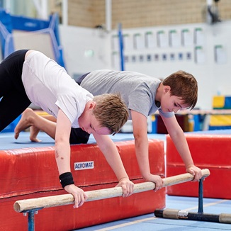 Two kids stretching out onto a gymnastics low bar at the Perth HPC Kids Gymnastics in Mount Claremont, Perth