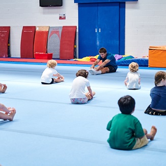 A group of kids spread out on the floor mats doing guided stretching at Perth HPC Kids Gym class